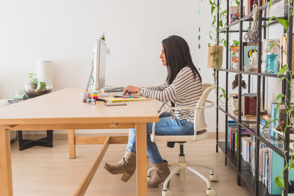 A woman sitting in her home office typing on her desktop computer.