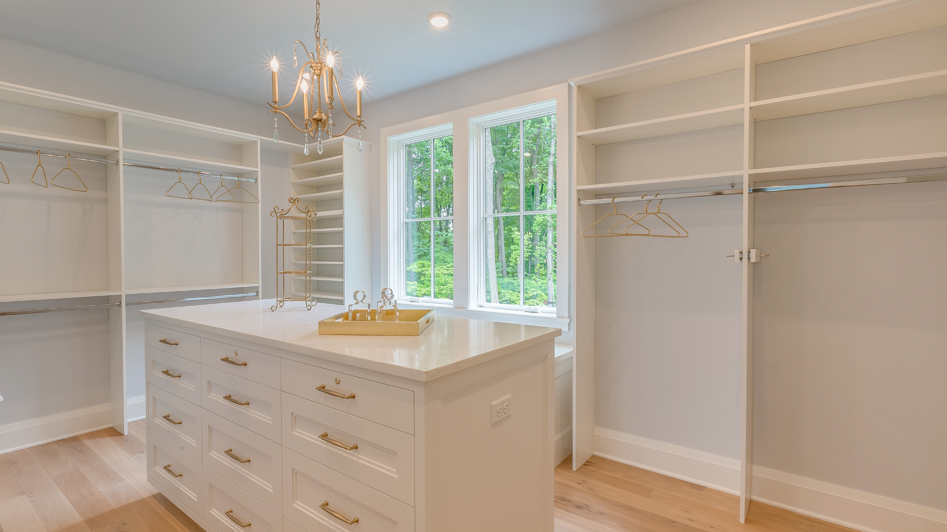 Luxury walk-in closet with a central island, gold hardware, and chandelier lighting