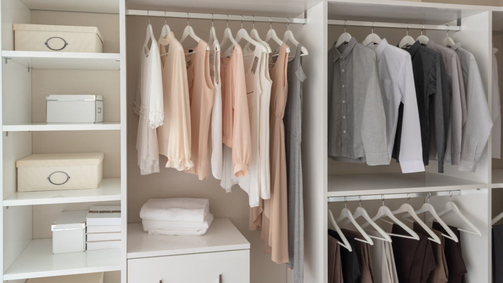 Neatly organized closet with hanging clothes and white shelving for storage.